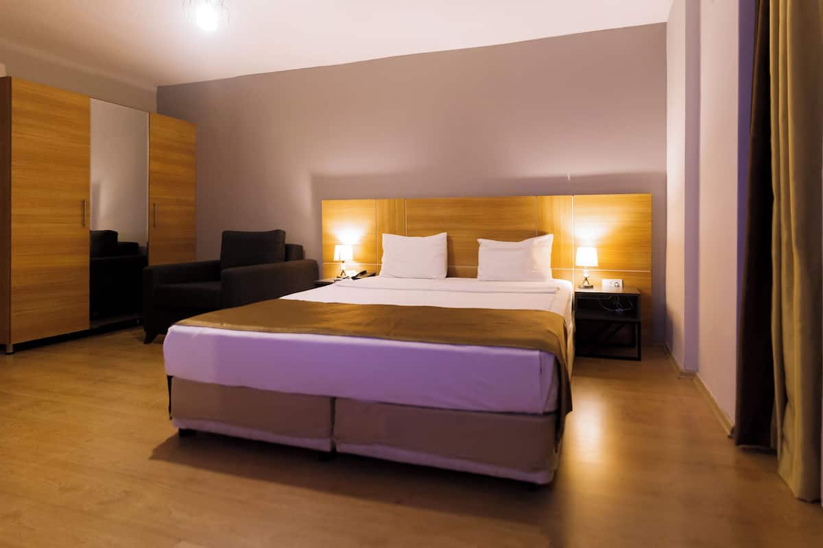 A hotel room with a large bed, a desk, a chair, and a wardrobe.