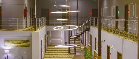 Un hall d’hôtel spacieux, doté d’un escalier central, de plusieurs espaces aménagés pour s’asseoir et d’un design moderne au niveau du plafond.