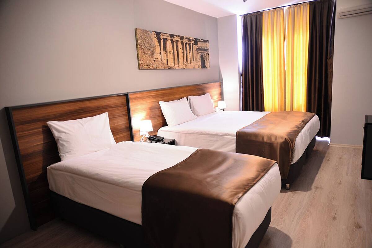 A hotel room with two beds, a wooden headboard, a nightstand with a lamp, and a painting on the wall.