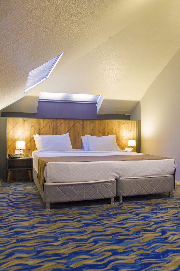 Habitación de hotel con una cama grande, dos mesitas de noche con lámparas, un cabecero de madera y una alfombra estampada.