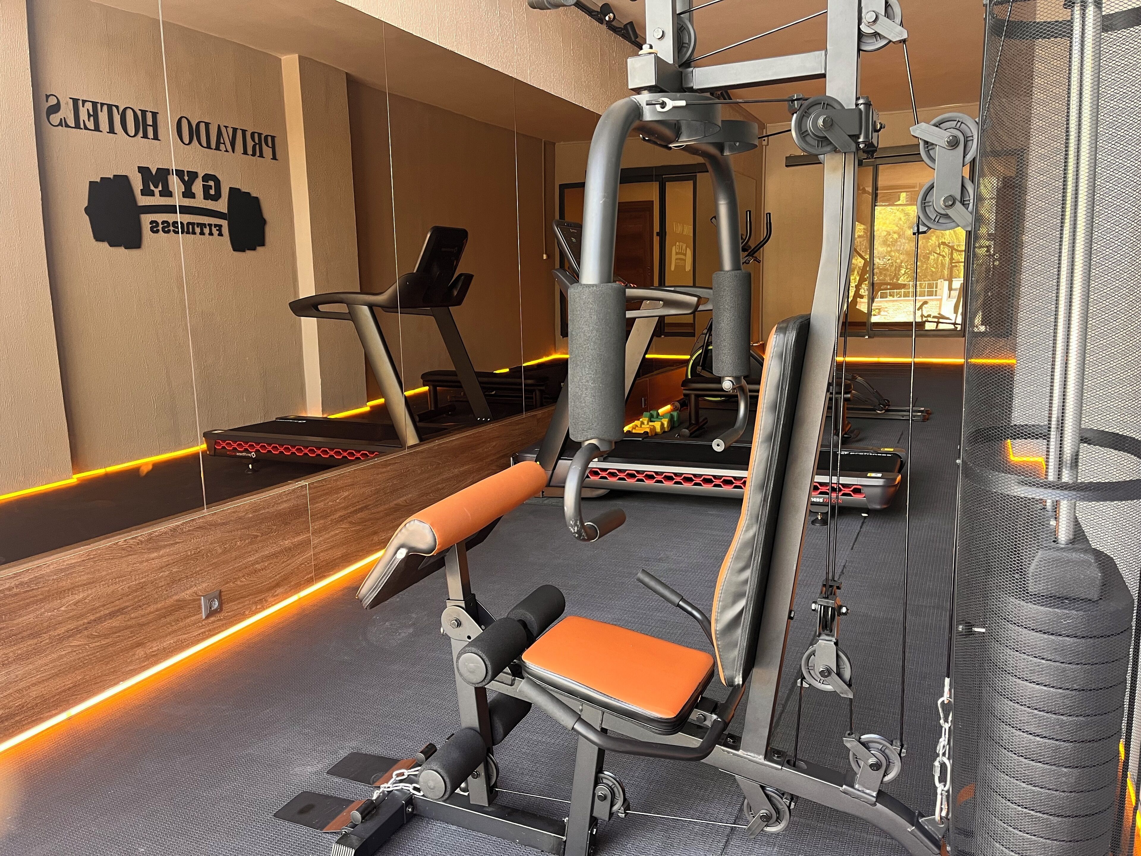 A gym with exercise equipment, a treadmill, and a wall with the text "BRIDGED HOTELS FITNESS".