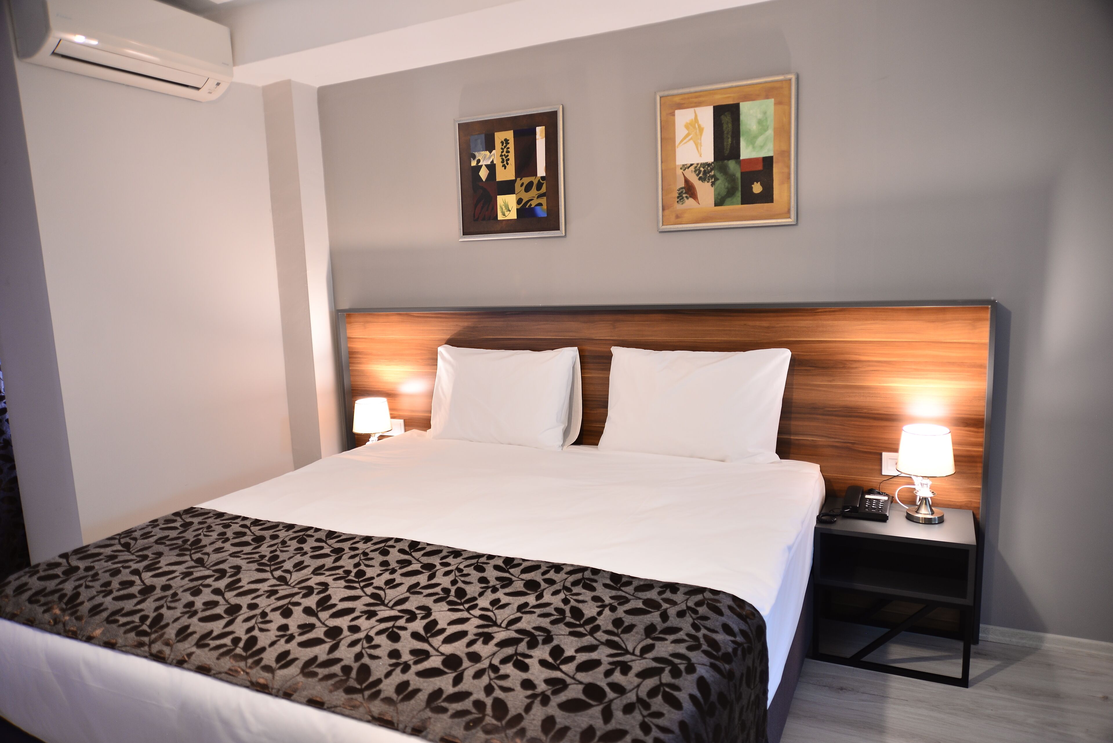 Een hotelkamer met een groot bed, twee nachtkastjes met lampen en twee abstracte schilderijen aan de muur.