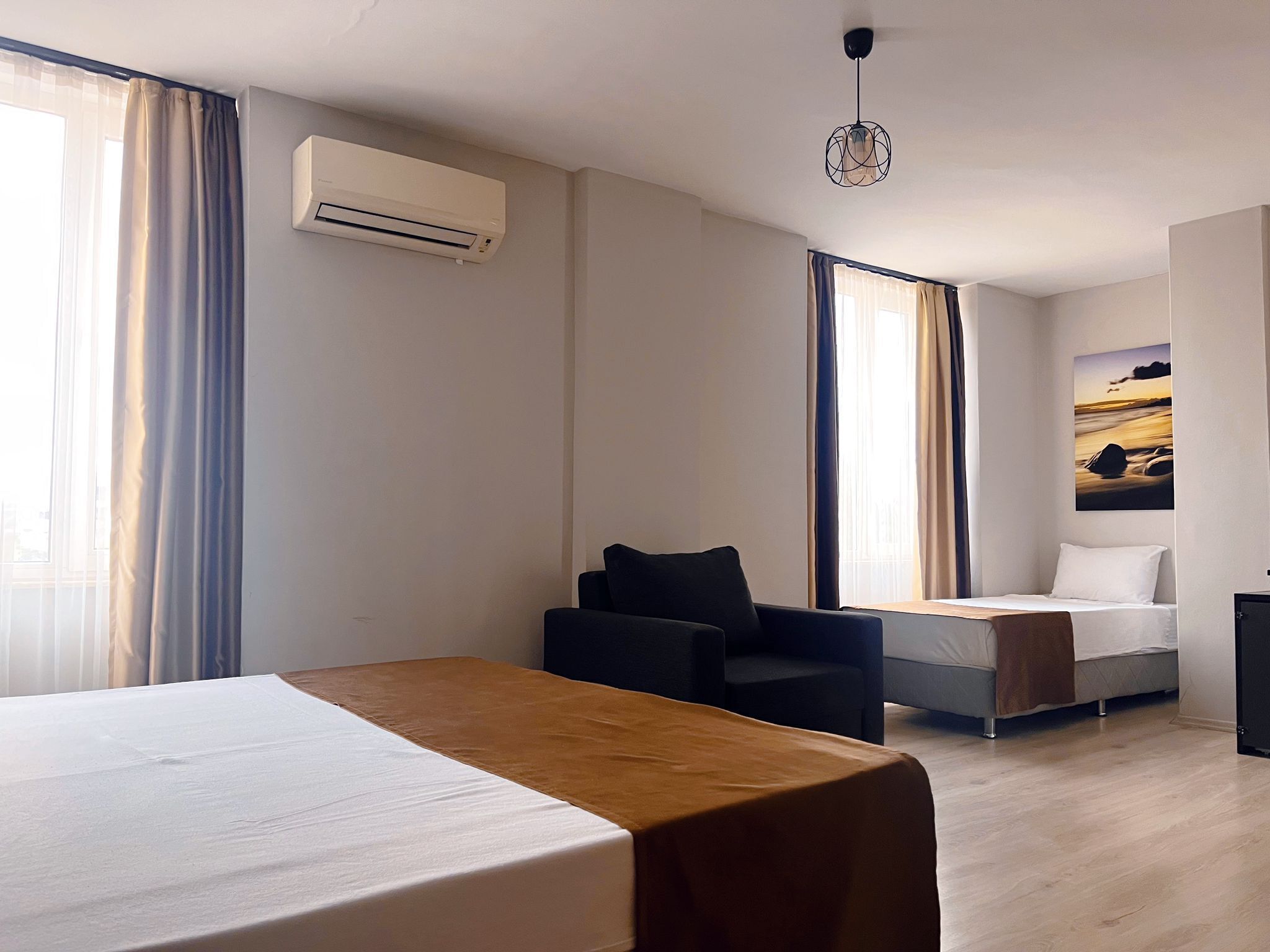 Habitación de hotel con cama, escritorio, sillón y sofá. Hay un equipo de aire acondicionado en la pared y un cuadro colgado en la pared.