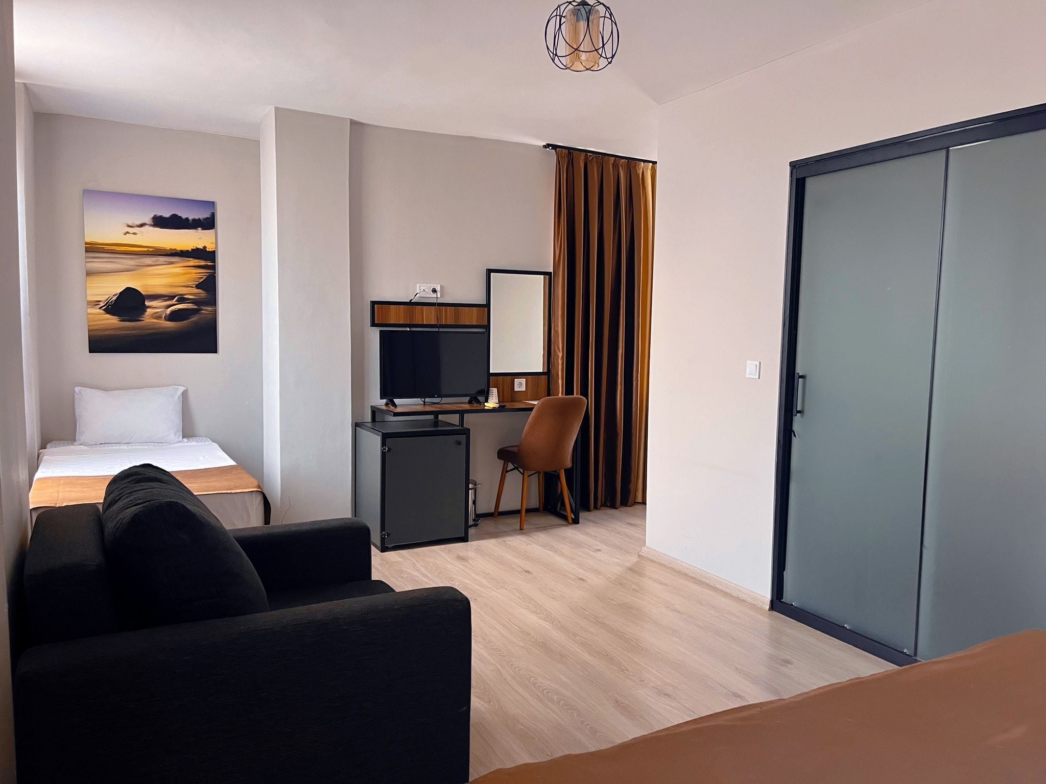 A hotel room with a bed, a desk with a computer, a chair, a wardrobe, and a painting on the wall.
