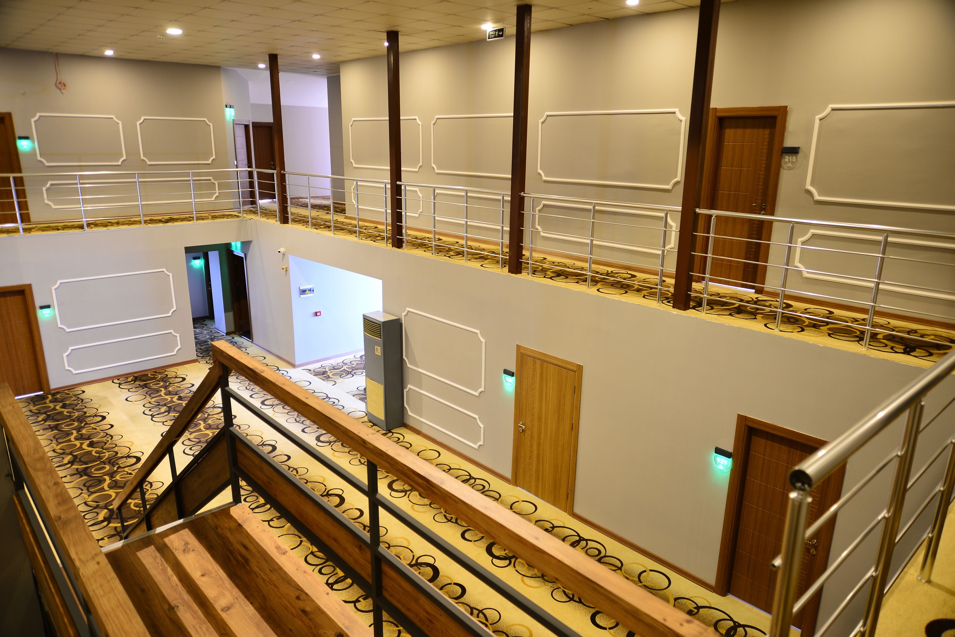 A hotel interior with a central staircase, multiple doors, and a patterned carpet.