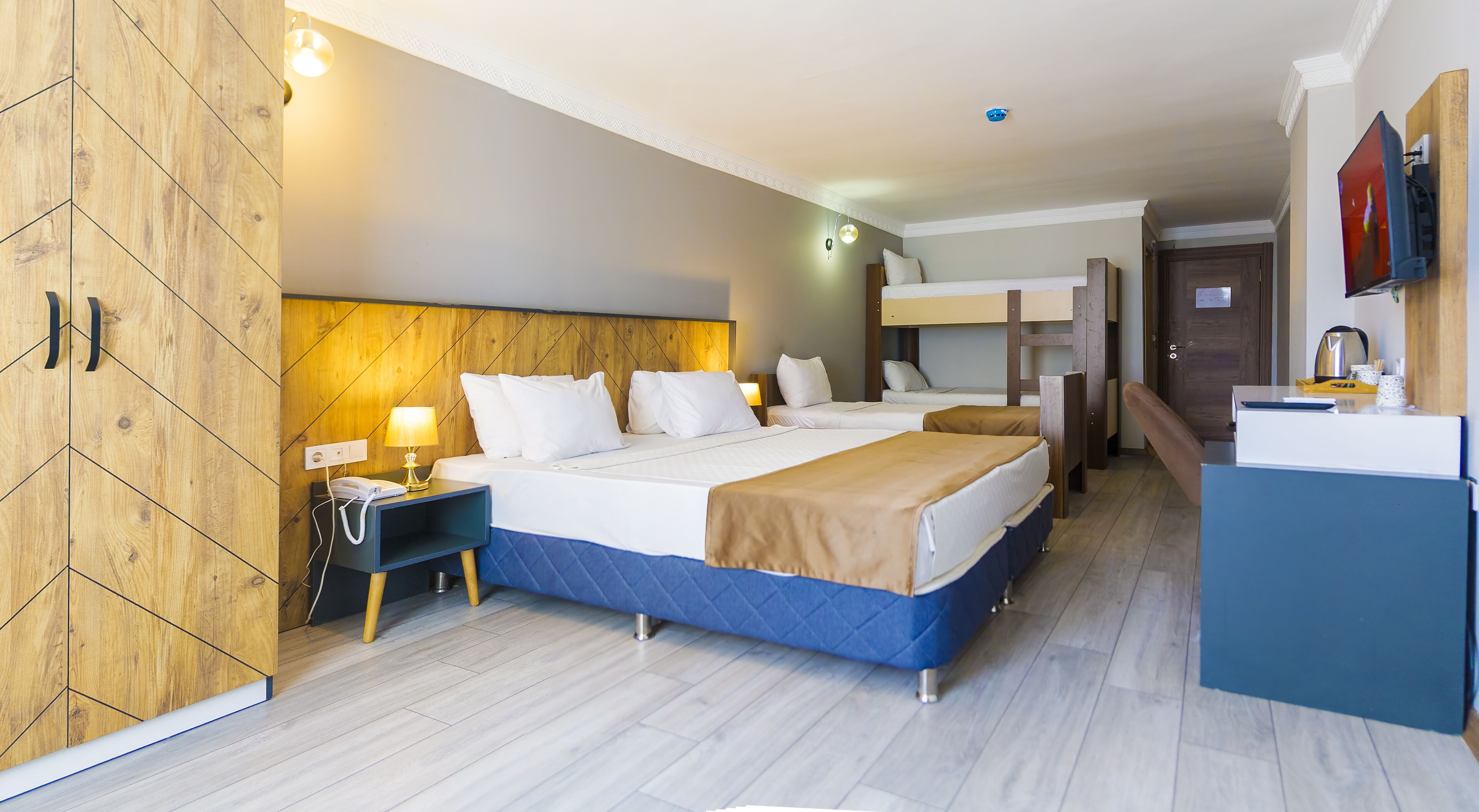 A hotel room with a large bed, a desk, a wardrobe, a television, and a kitchenette.