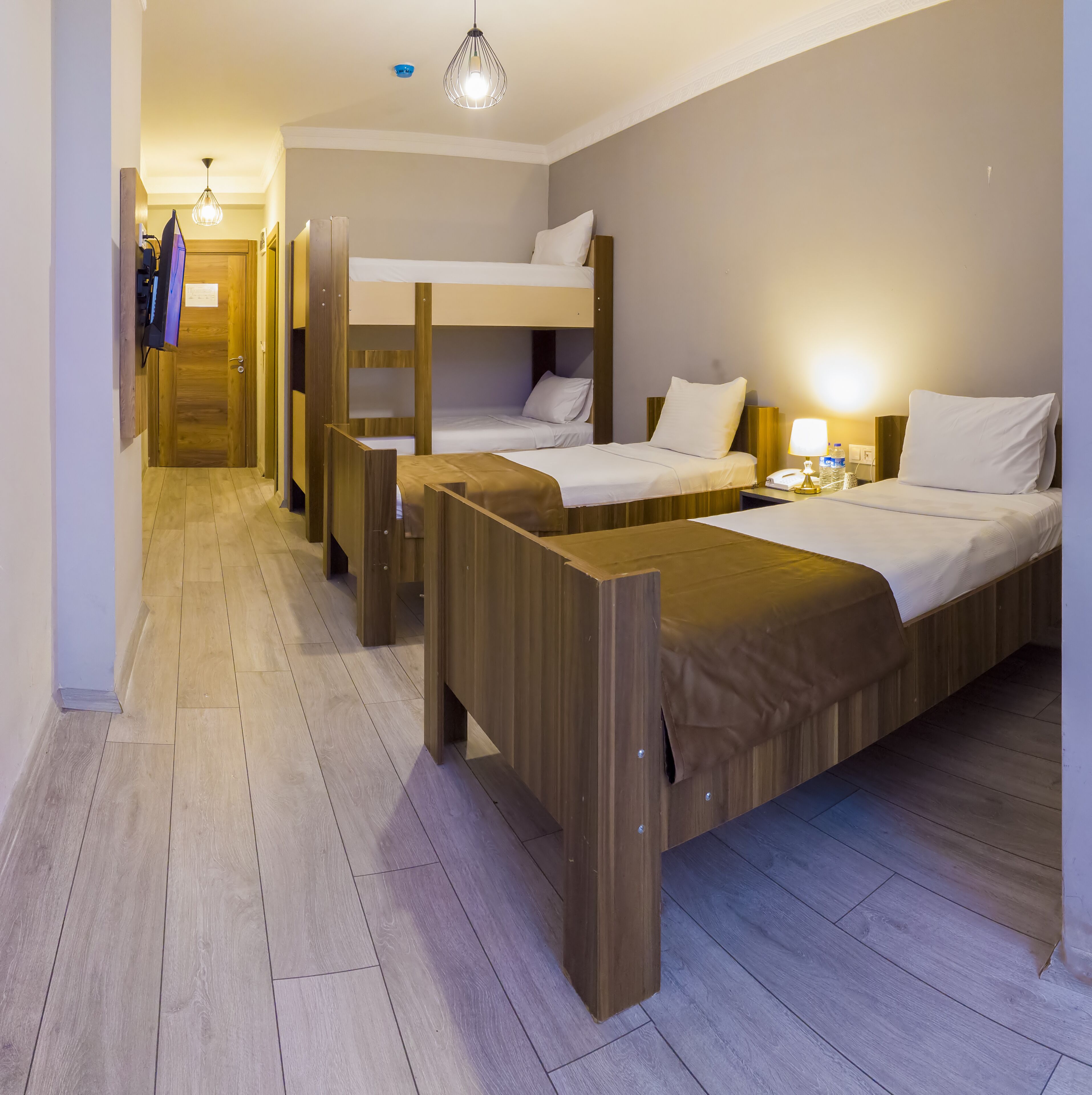 A hotel room with bunk beds, wooden furniture, a flat-screen TV, and a bedside table with a lamp and water bottle.