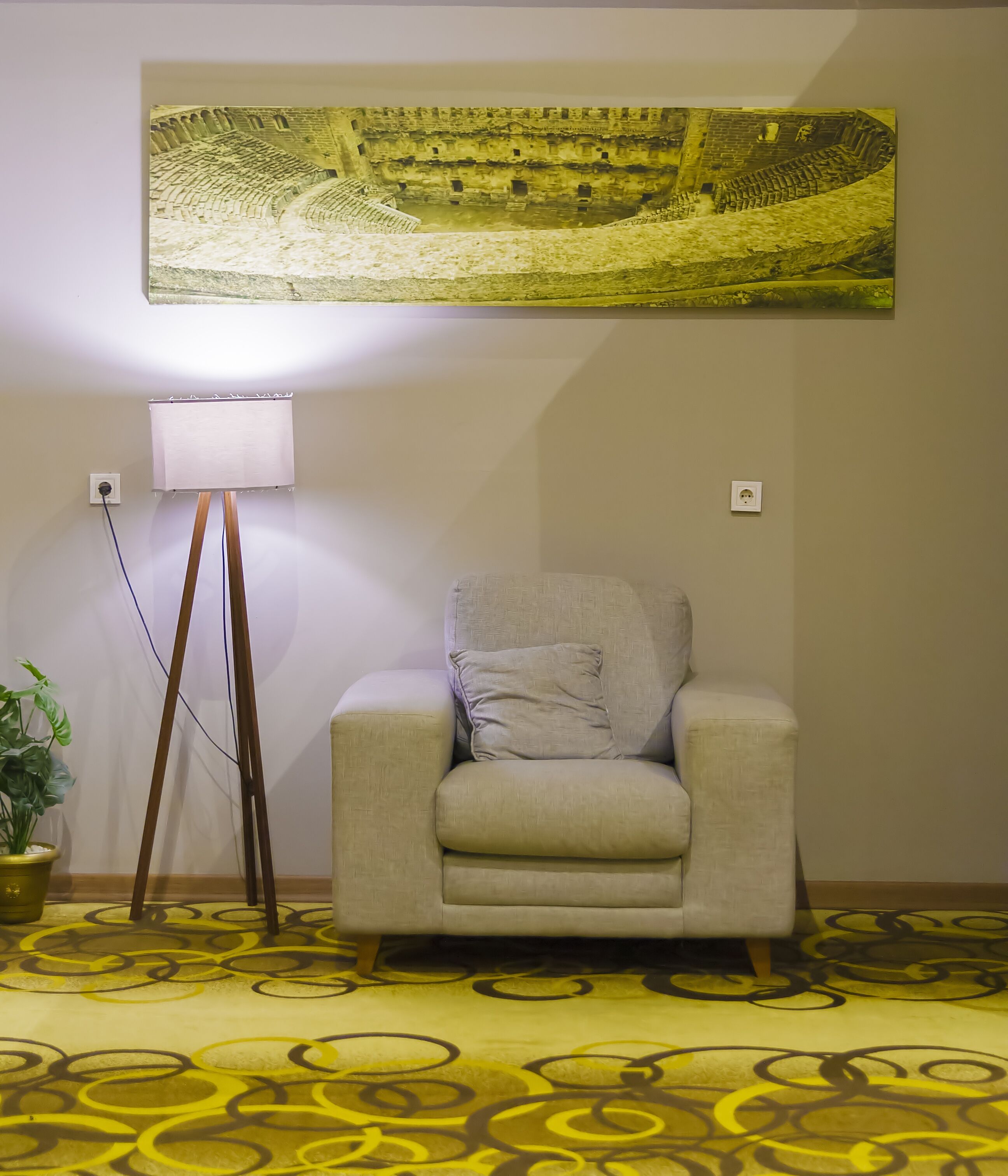 Una habitación con sofá, lámpara de pie, planta en maceta y un cuadro grande en la pared.