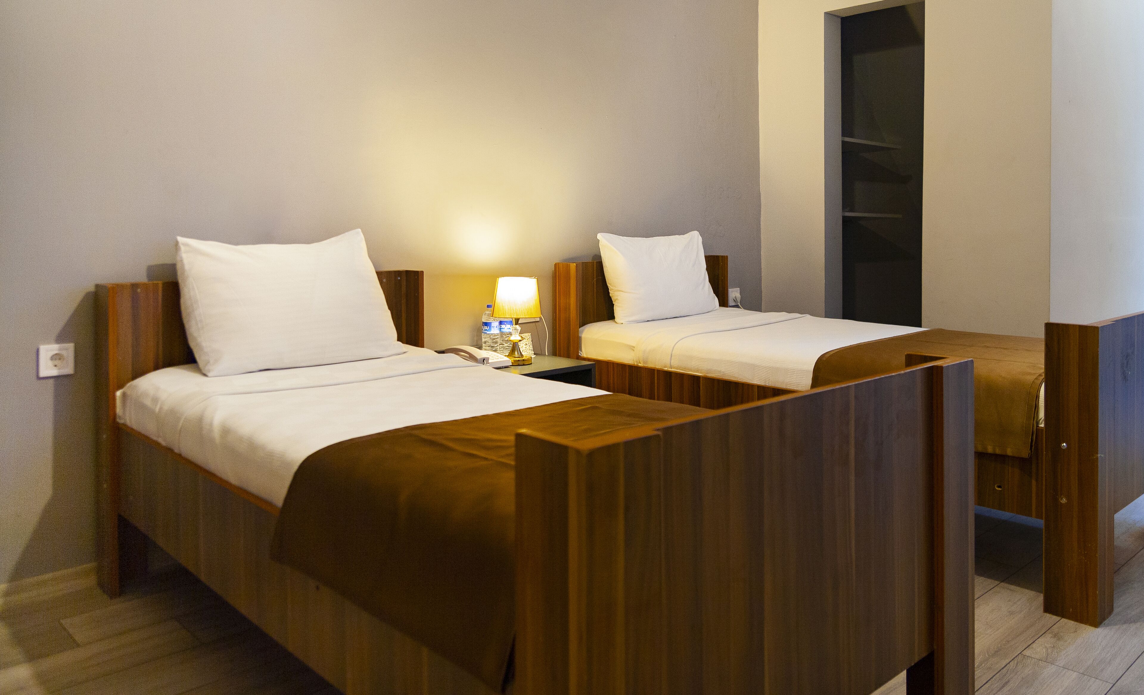 Habitación de hotel con dos camas de madera, una mesita de noche con lámpara y una pequeña mesa entre las camas.