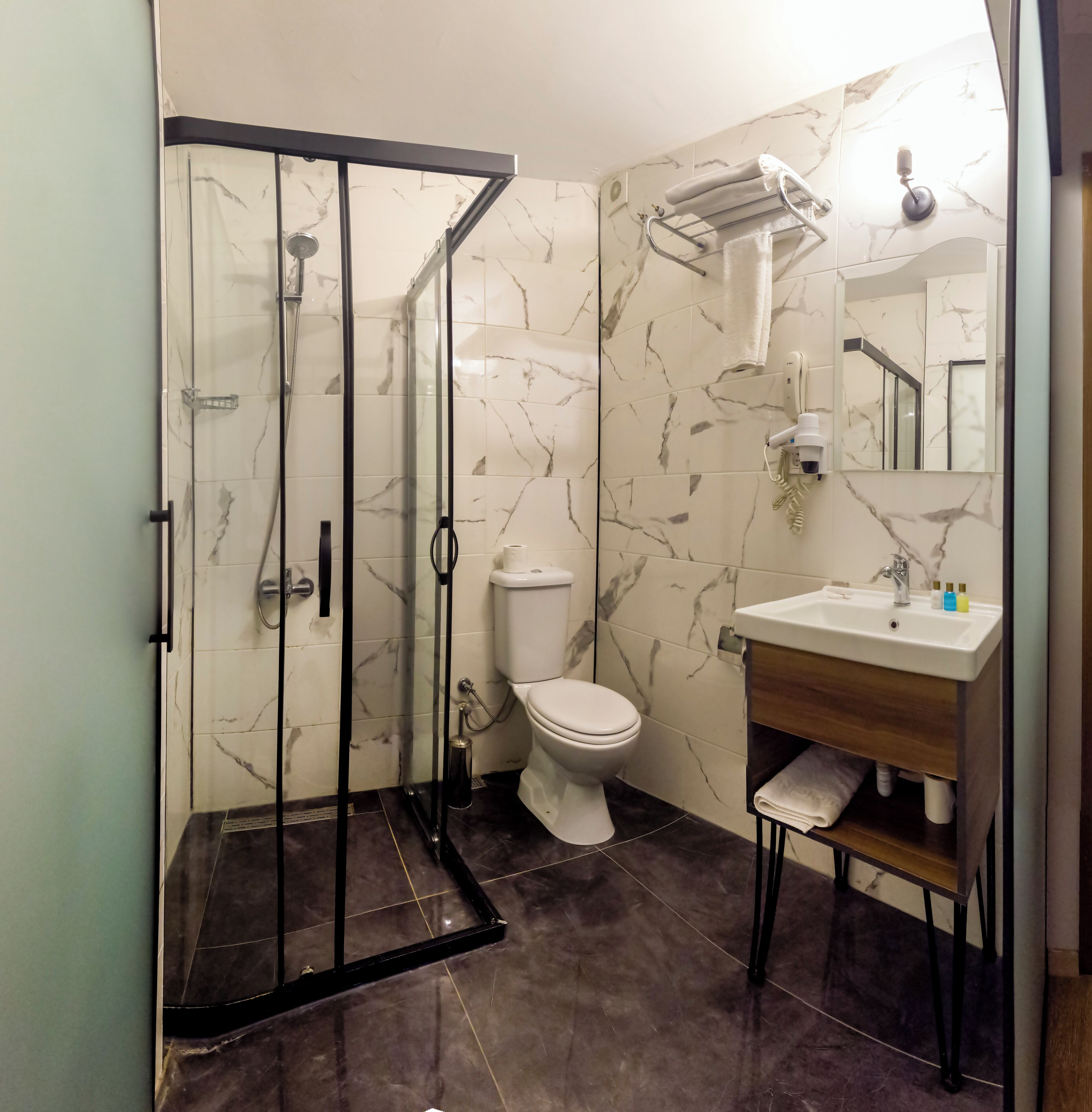 A modern bathroom with a glass-enclosed shower, a toilet, and a sink with a wooden vanity.
