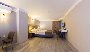 Una habitación de hotel moderna con cama, escritorio, silla, televisor y una pequeña cocina.