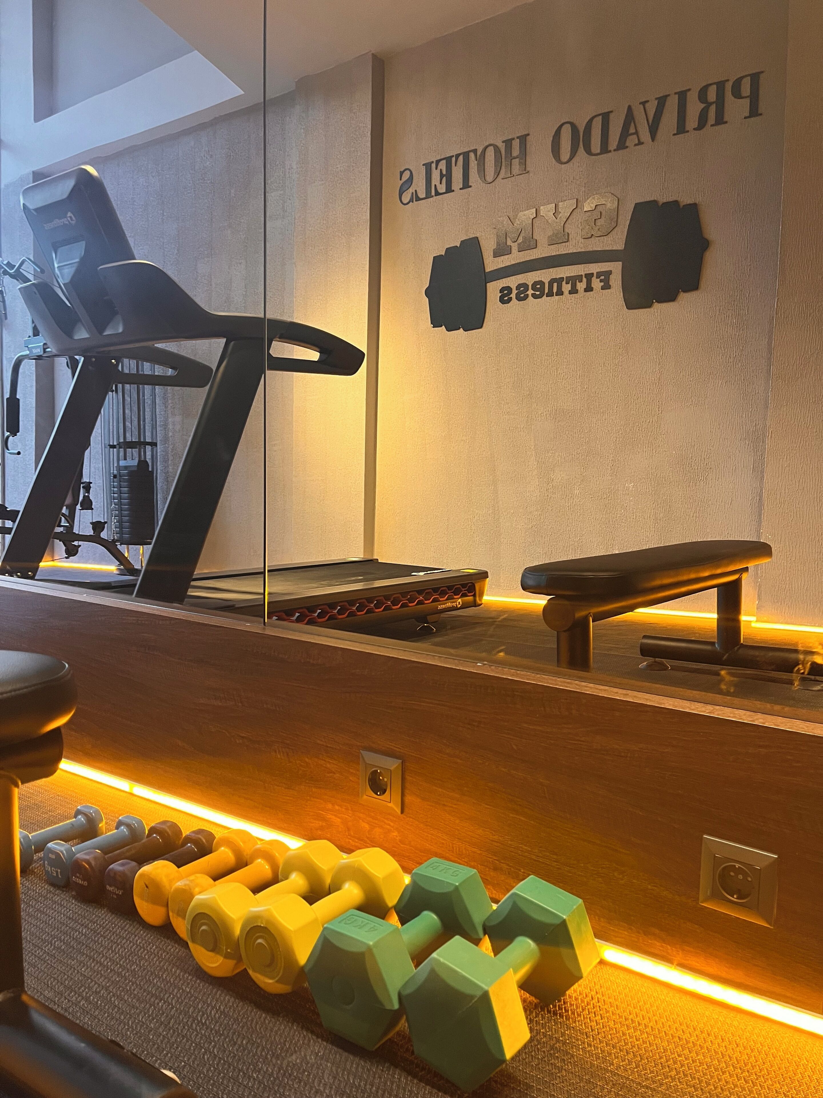 Een sportschool met een loopband, een gewichtbank en gewichtsschijven.