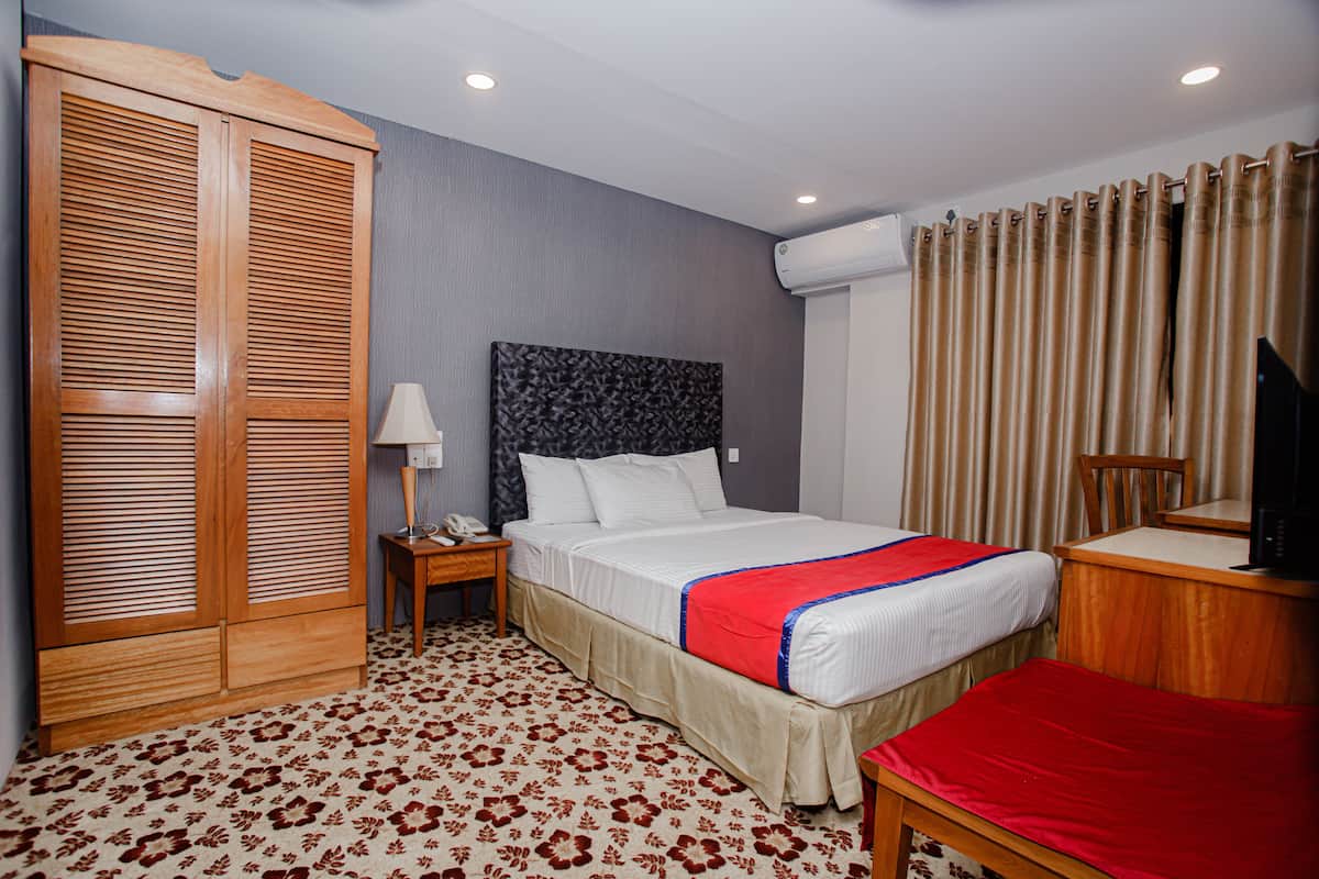 A hotel room with a bed, a desk, a chair, a wardrobe, and an air conditioning unit.