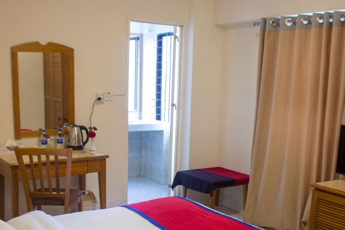 A hotel room with a bed, a desk, a chair, a small table, a mirror, and a view of the outside.