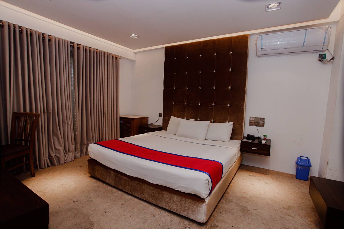 A hotel room with a large bed, a wooden headboard, a nightstand, a desk, and a chair.
