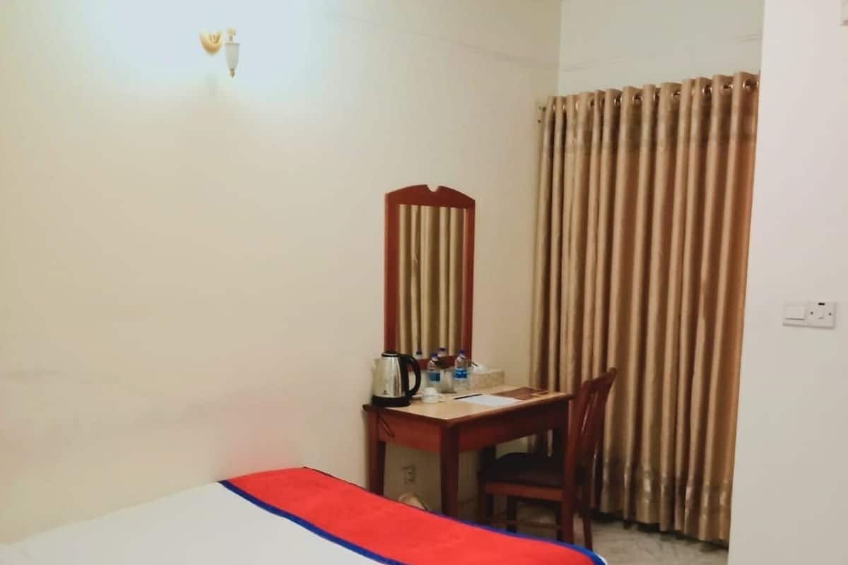 A hotel room with a bed, a desk, a chair, and a window with curtains.