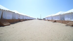 Une plage de sable bordée de rangées de tentes blanches.