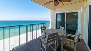 A balcony with a table and chairs, a ceiling fan, a glass door leading to a room, and a view of the beach and ocean. - Seas The Day Regency Towers 1122-Beachfront-Beautiful Decor. Fantastic Views! (Panama City)