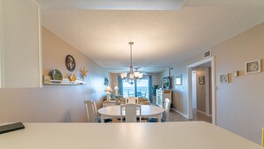 A dining area with a round table, chairs, a chandelier, and a view of the outside. - Seas The Day Regency Towers 1122-Beachfront-Beautiful Decor. Fantastic Views! (Panama City)