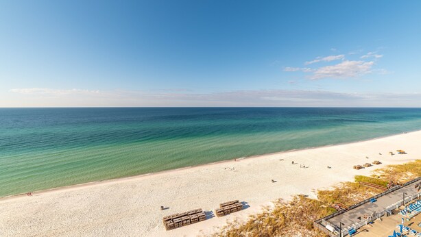 A beach with clear turquoise water, white sand, and a few beachgoers. There are wooden structures and a covered area with blue chairs. - Seas The Day Regency Towers 1122-Beachfront-Beautiful Decor. Fantastic Views! (Panama City)