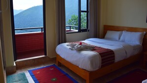 A hotel room with a bed, a window with a view of mountains, and a red and blue rug on the floor.