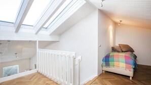 Et soveværelse med skrå vægge, en hvid radiator og et farverigt tæppe på sengen.