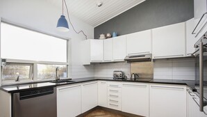 Et moderne køkken med hvide skabe, en rustfri opvaskemaskine, en brødrister og en elkedel på bordpladen.