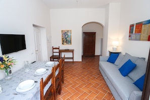 A dining area with a table set for four, a sofa with blue cushions, and a TV mounted on the wall. - gorgeous terrace in Florence (Firenze)