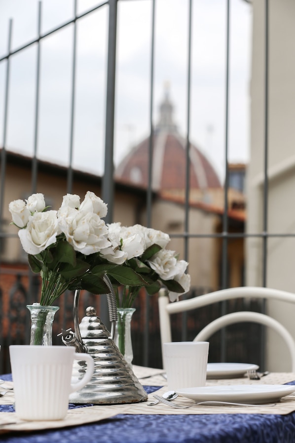 A dining table with white tableware, a metal teapot, and a vase with white flowers. - gorgeous terrace in Florence (Firenze)