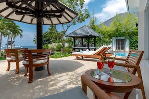A wooden outdoor seating area with a glass table, two lounge chairs, and a gazebo.