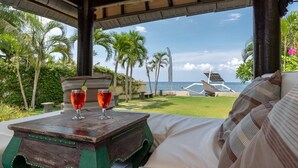 A cozy outdoor seating area with a view of the ocean, a wooden table with two glasses, and a lounge chair.