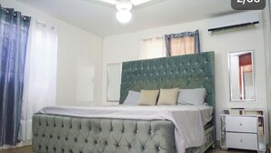 Ein Schlafzimmer mit einem karomanischen Kopfteil, einem Bett mit weißen Bettwäsche, einem Nachttisch und einem Spiegel.