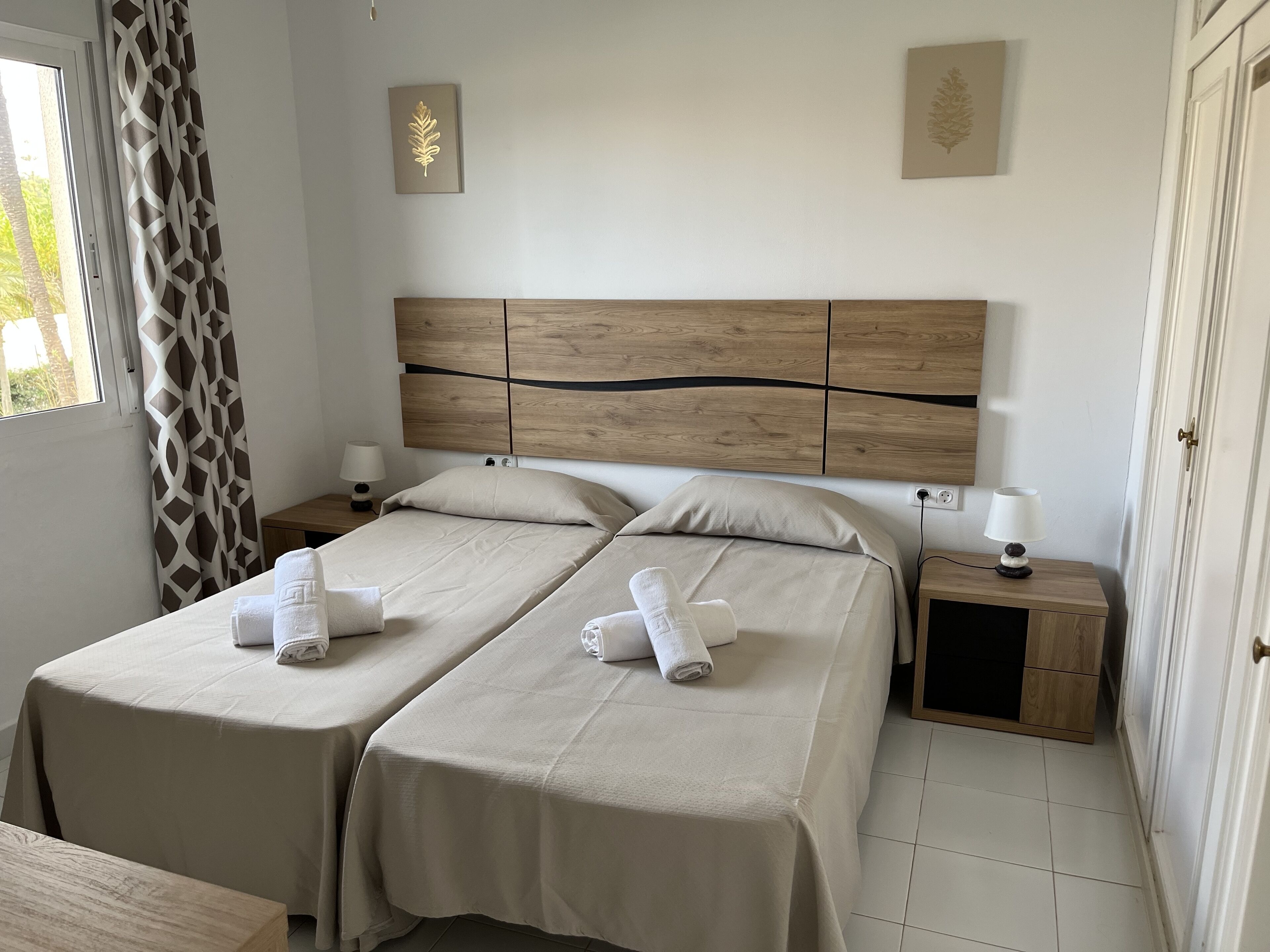 Une chambre double avec deux lits, chacun doté d’une tête de lit en bois, de draps blancs et d’une table de chevet avec une lampe.