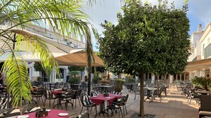 Area caffè all'aperto con tavoli e sedie, circondata da piante e elementi architettonici.