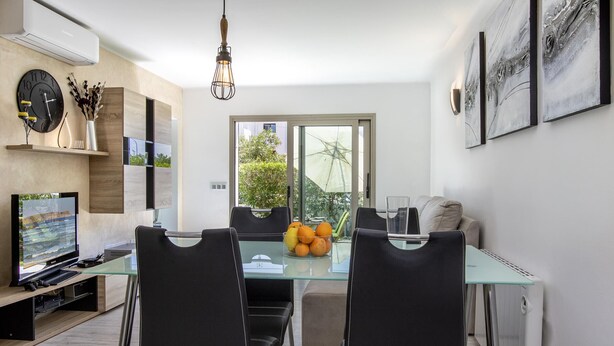 A modern living room with a glass dining table, black chairs, a flat-screen TV, and a large window with a view of greenery. - VISTA MONTE ( Francisca ). Apartment in residentail area near The beach. (Puerto Pollensa)