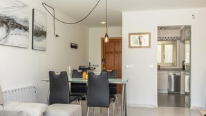 A modern living room with a sofa, a glass coffee table, and a dining area with a glass table and chairs. There is a kitchen visible in the background with a dishwasher and cabinets. - VISTA MONTE ( Francisca ). Apartment in residentail area near The beach. (Puerto Pollensa)