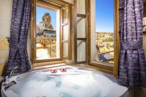 A bathroom with a bathtub, a window with a view of a historic building, and purple curtains.