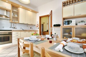 Une cuisine avec des meubles en bois, un four à micro-ondes, une cuisinière et une table à manger mise avec des assiettes, des tasses et un saladier rempli de fruits.