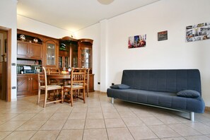 Un salon avec un canapé bleu foncé, une table à manger en bois, des chaises et un coin cuisine doté de meubles en bois et d’un four encastré.