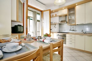 A modern kitchen with wooden cabinets, a dining table set with plates, cups, and a bowl of fruit.