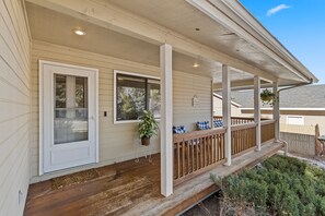 A covered porch with a wooden railing, a door, and a potted plant.