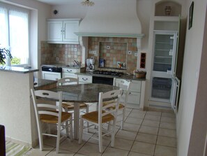 A kitchen with white cabinets, a tiled backsplash, a stove, and a dining area with chairs and a table.