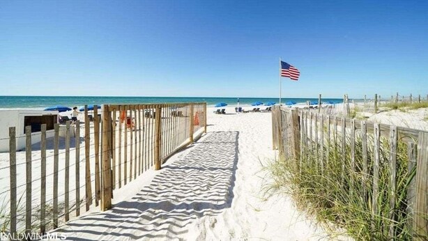 Ein Sandweg am Strand, mit Holzzaun und einer amerikanischen Flagge.