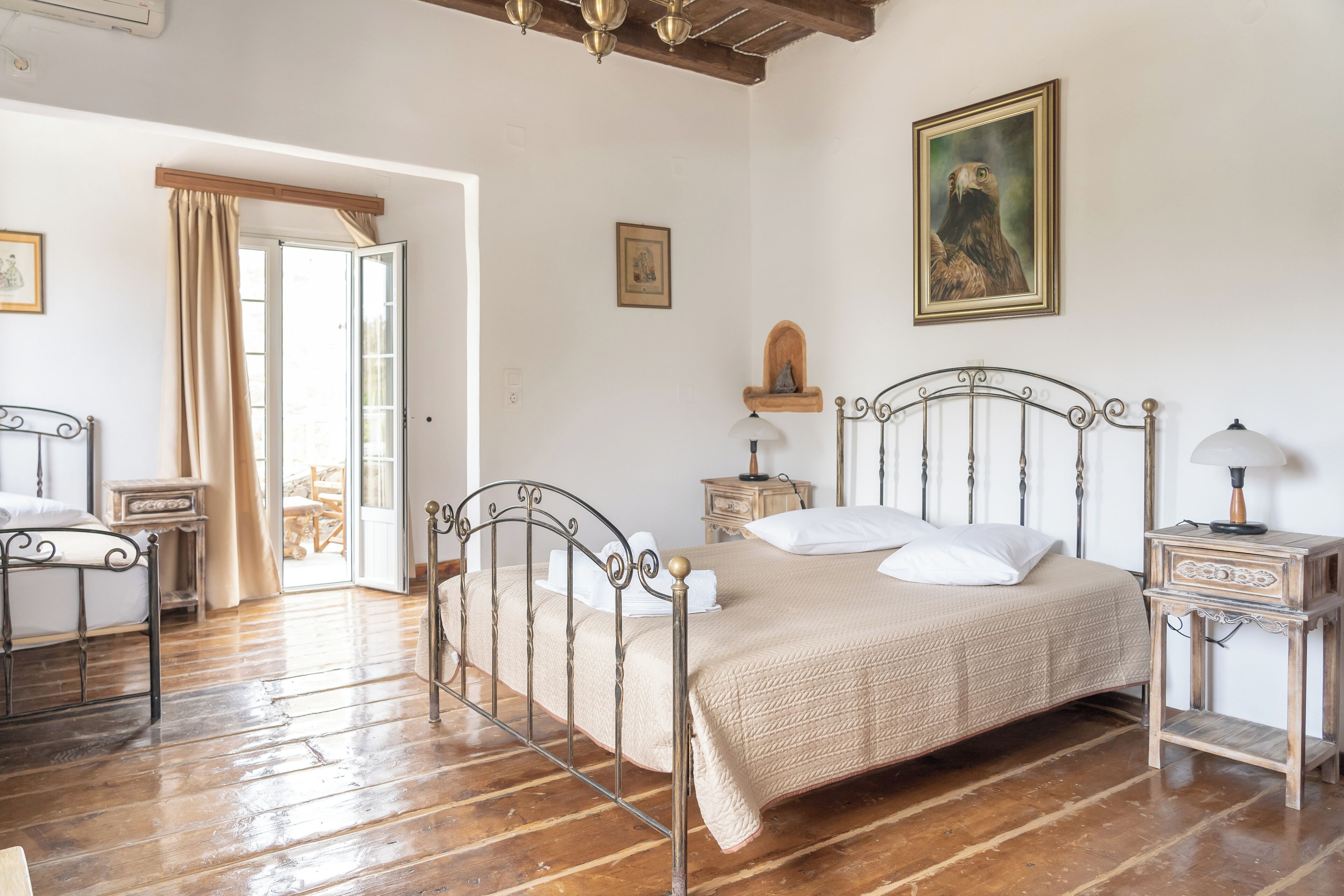 A bedroom with a metal bed frame, a wooden floor, a bedside table with a lamp, and a painting on the wall.