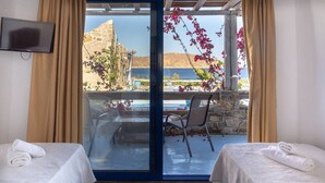 Una stanza con due letti, televisione e vista sul mare tramite una porta in vetro.