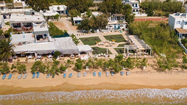 Vista aerea di un resort costiero con spiaggia, lettini e area piscina.