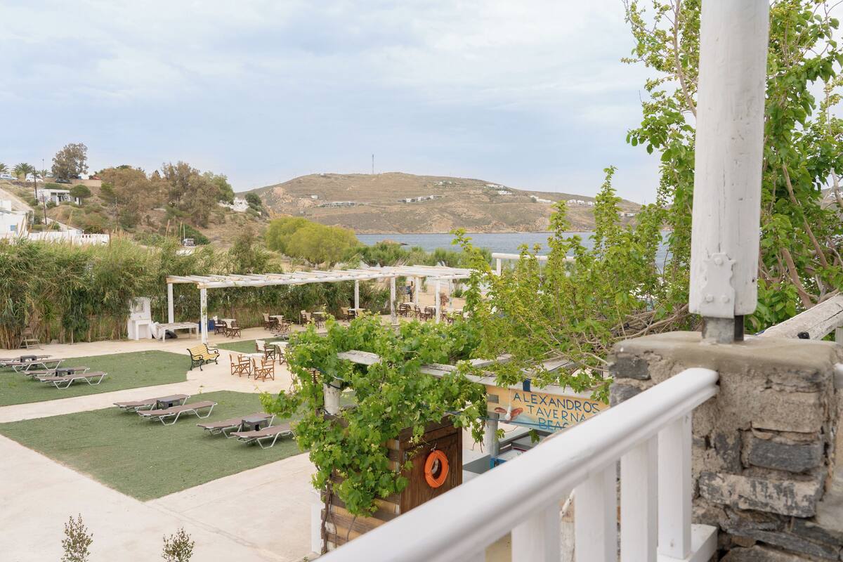 A terrace with outdoor seating and a view of a hill and water.