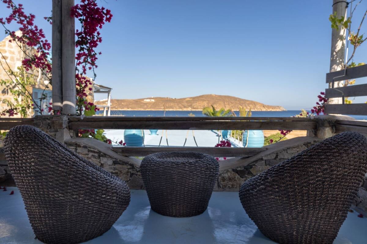 A terrace with wicker furniture, a view of the sea, and a mountainous landscape in the background.