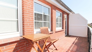 A patio with a wooden table and chairs, a brick wall, and a white door. - Centrally located apartment for 4 people and dog (Greetsiel)