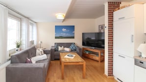 A living room with a grey sofa, a wooden coffee table, a TV, and a white refrigerator. - Centrally located apartment for 4 people and dog (Greetsiel)